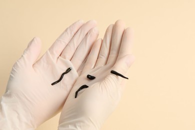 Photo of Woman holding medicinal leeches on pale yellow background, closeup. Space for text