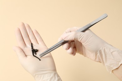 Photo of Woman holding medicinal leeches and tweezers on pale yellow background, closeup