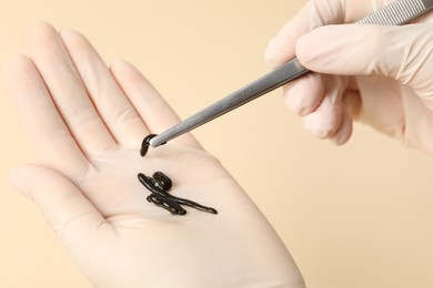 Photo of Woman holding medicinal leech with tweezers on pale yellow background, closeup