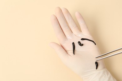 Photo of Woman holding medicinal leech with tweezers on pale yellow background, top view. Space for text