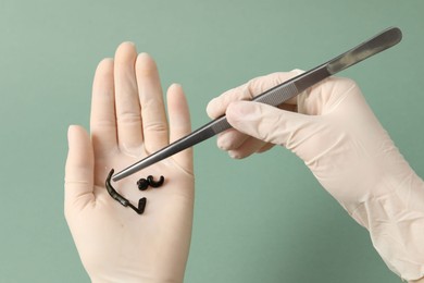 Photo of Woman holding medicinal leech with tweezers on green background, closeup