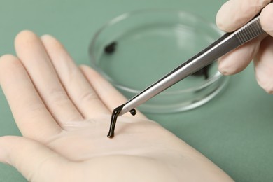 Woman holding medicinal leech with tweezers on green background, closeup