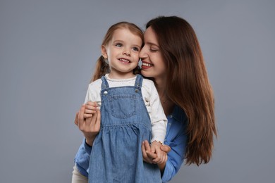 Happy mother with her cute little daughter on grey background