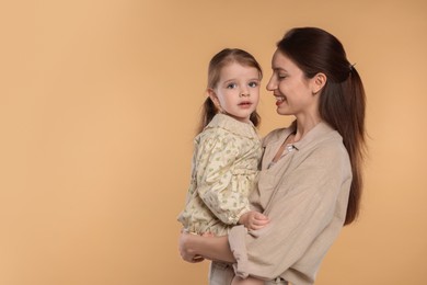 Happy mother with her cute little daughter on beige background, space for text