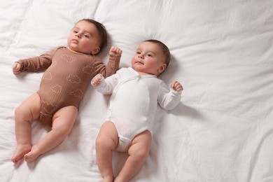 Photo of Cute twin babies resting on bed indoors, top view. Space for text