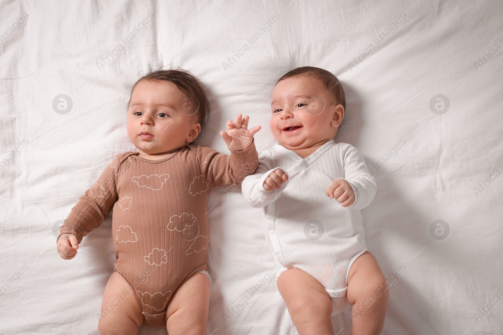 Photo of Cute twin babies resting on bed indoors, top view