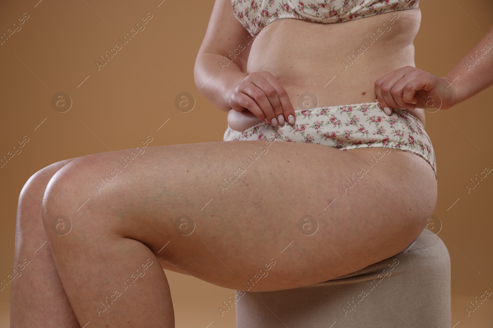 Photo of Woman with cellulite on pouf against dark beige background, closeup