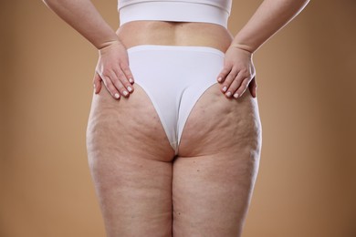 Photo of Woman with cellulite on light brown background, closeup