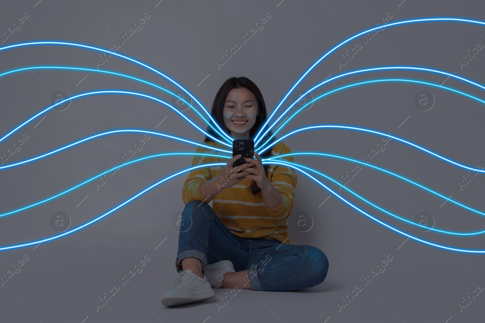 Image of Happy woman using mobile phone on grey background. Bright lines coming out of device symbolizing high speed internet