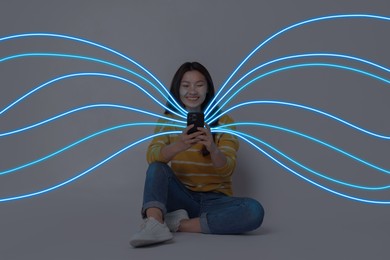 Image of Happy woman using mobile phone on grey background. Bright lines coming out of device symbolizing high speed internet