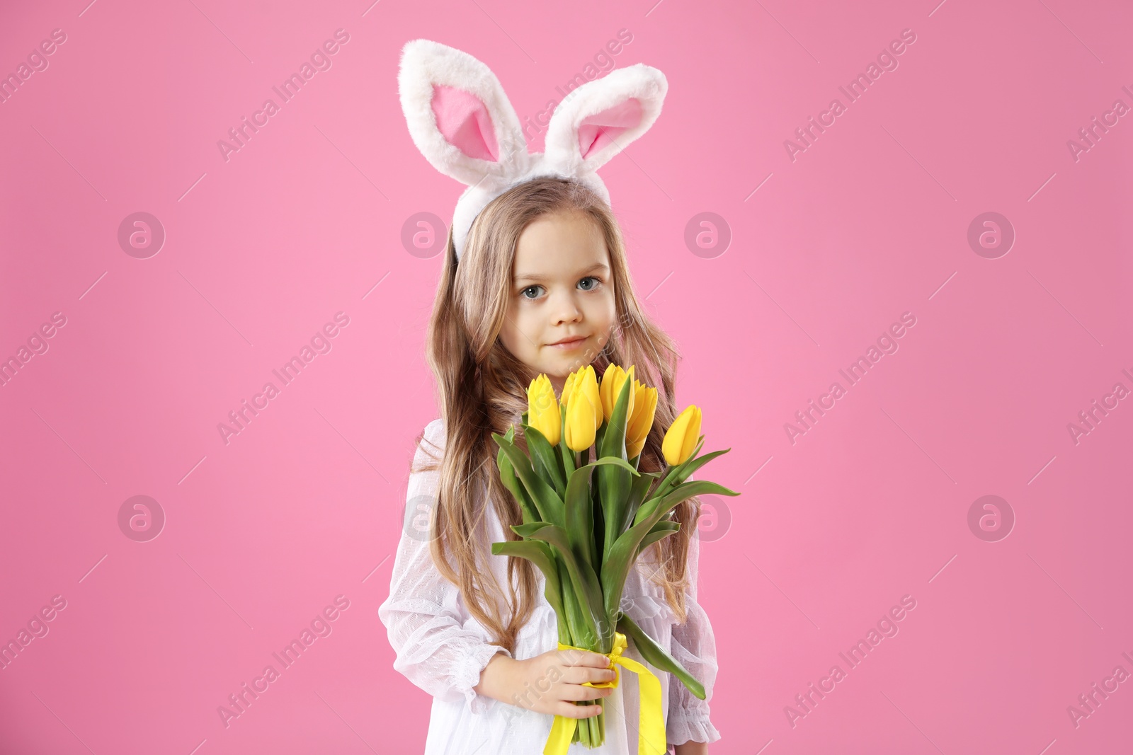 Photo of Cute little girl with bunny ears and tulips on pink background. Easter celebration