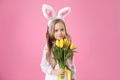 Cute little girl with bunny ears and tulips on pink background. Easter celebration