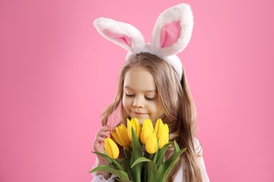 Photo of Cute little girl with bunny ears and tulips on pink background. Easter celebration