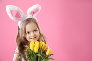 Cute little girl with bunny ears and tulips on pink background, space for text. Easter celebration