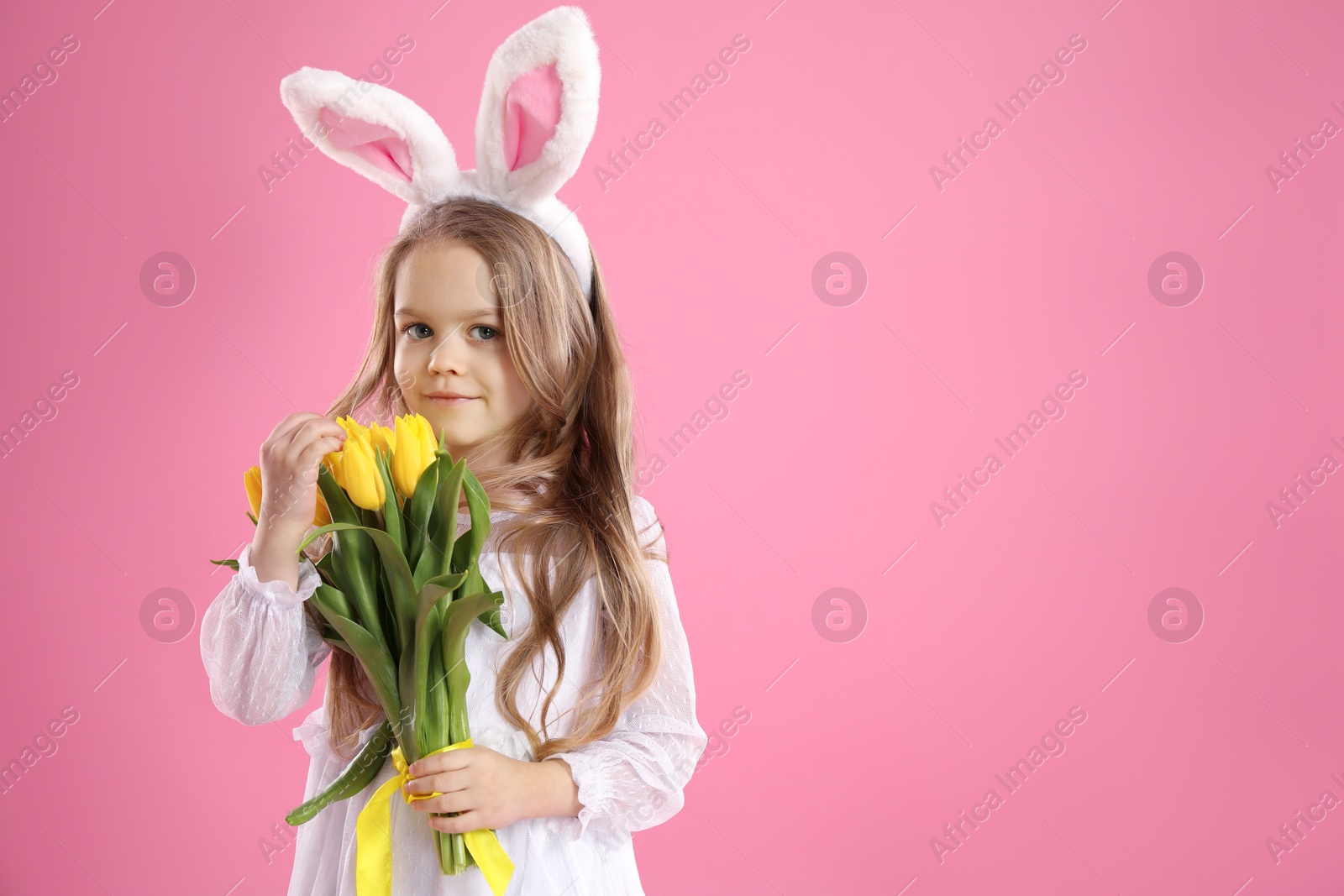 Photo of Cute little girl with bunny ears and tulips on pink background, space for text. Easter celebration