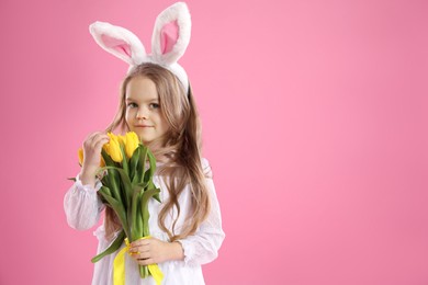 Photo of Cute little girl with bunny ears and tulips on pink background, space for text. Easter celebration