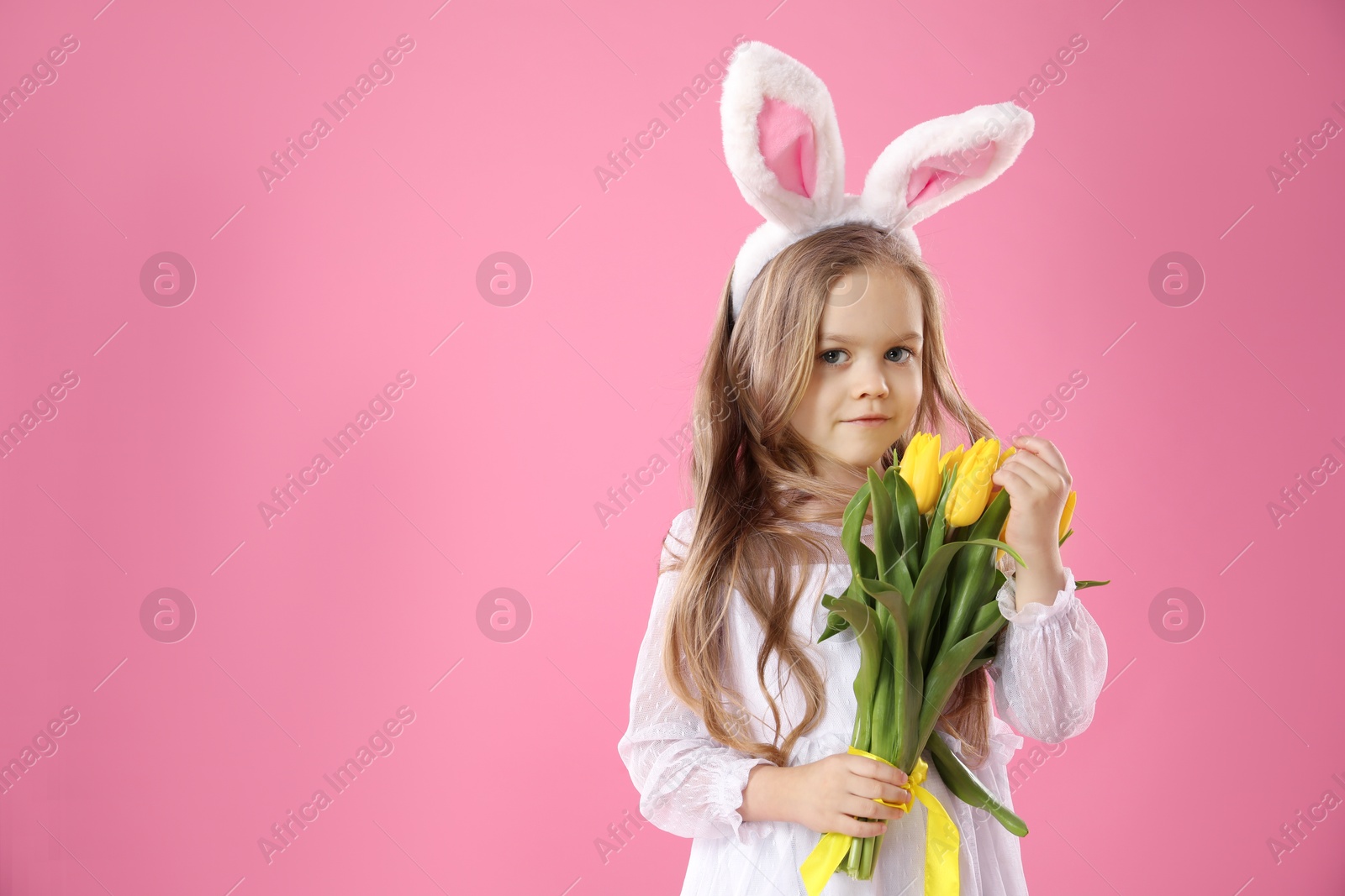 Photo of Cute little girl with bunny ears and tulips on pink background, space for text. Easter celebration