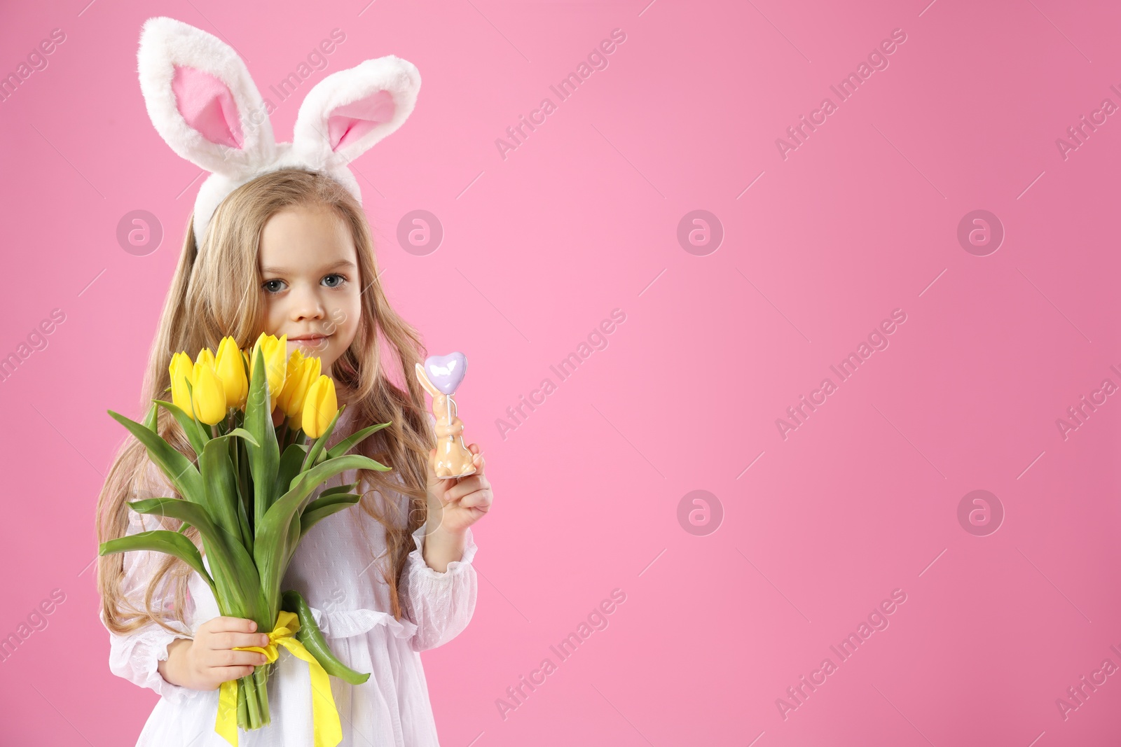 Photo of Cute little girl with bunny ears and tulips on pink background, space for text. Easter celebration