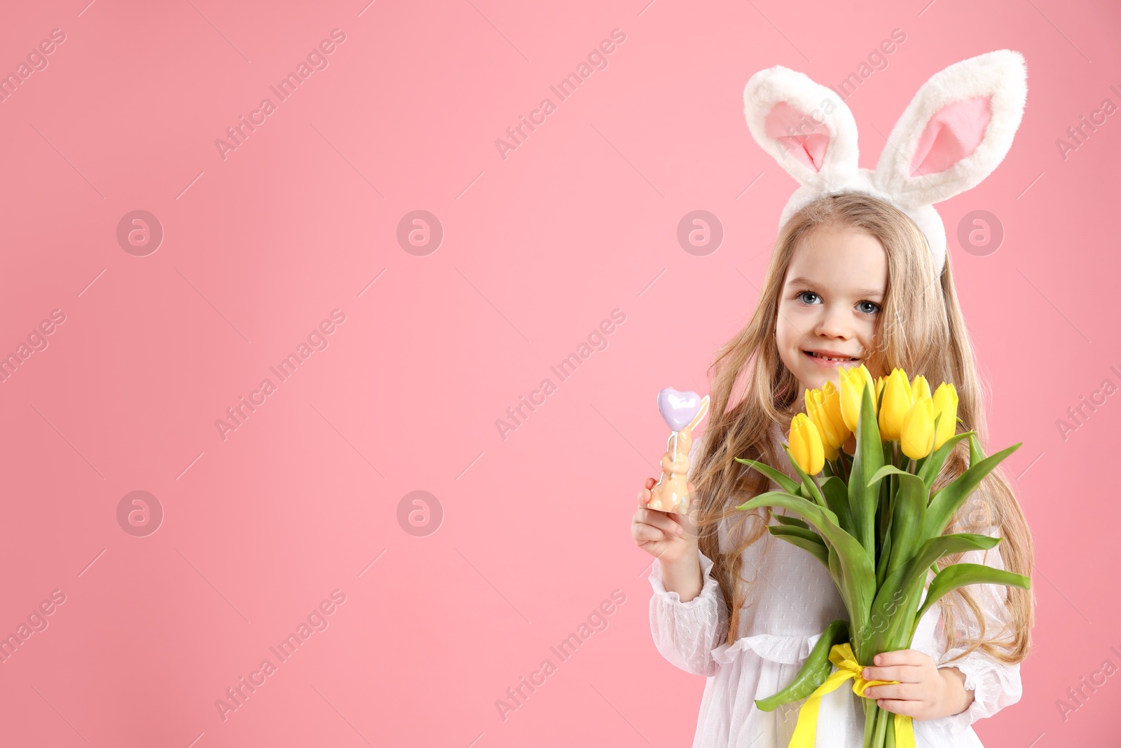 Photo of Cute little girl with bunny ears and tulips on pink background, space for text. Easter celebration