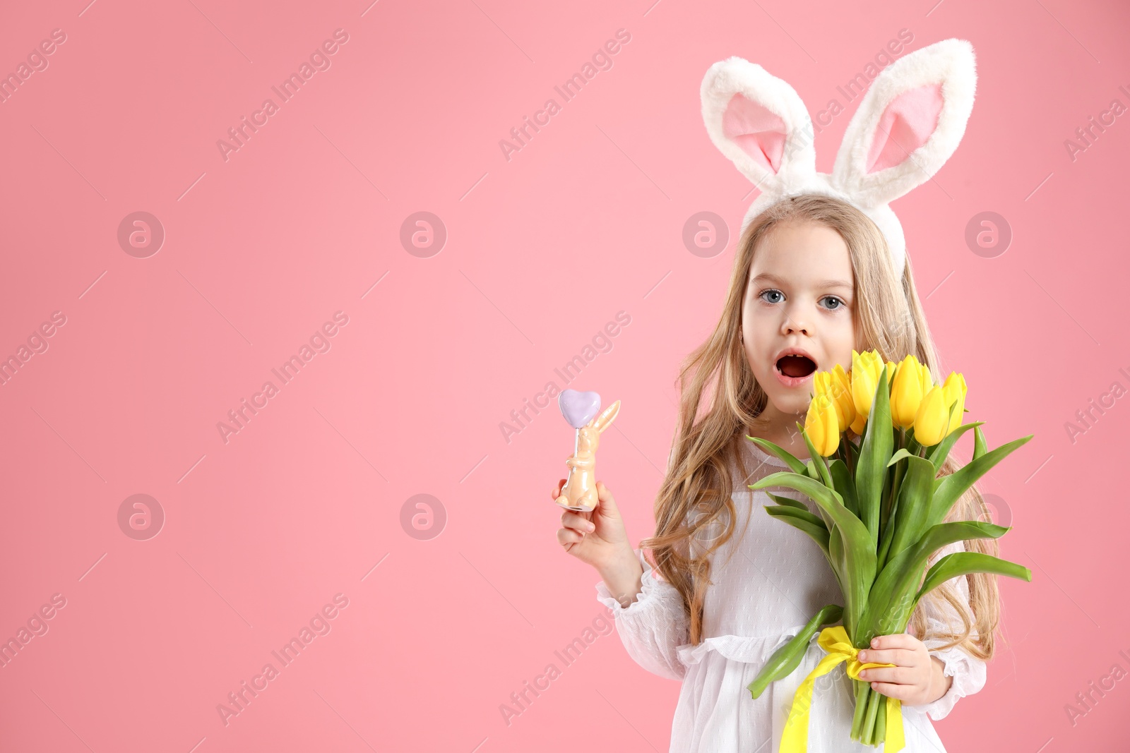 Photo of Cute little girl with bunny ears and tulips on pink background, space for text. Easter celebration