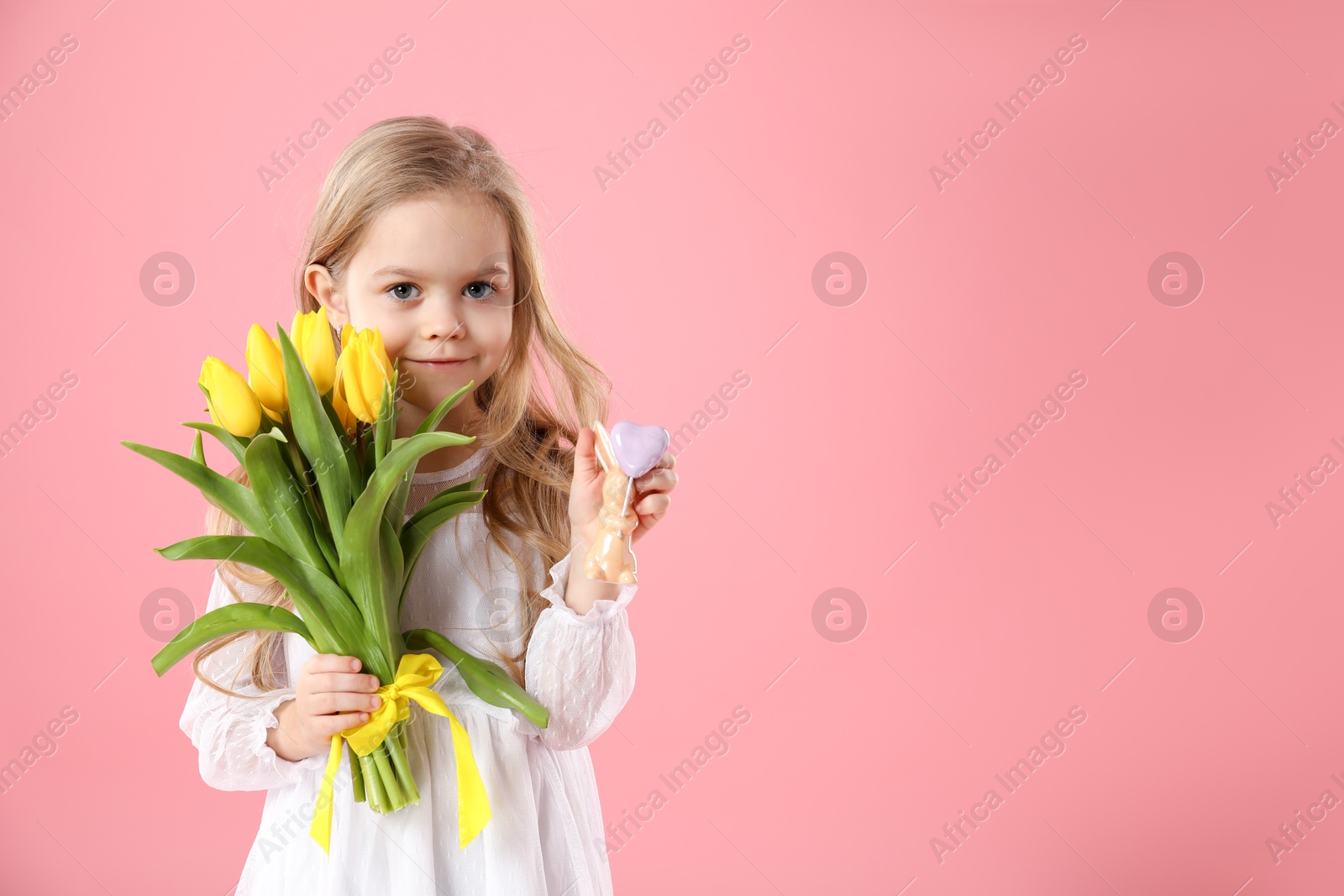 Photo of Cute little girl with yellow tulips and decorative bunny on pink background, space for text. Easter celebration