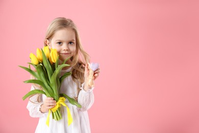 Cute little girl with yellow tulips and decorative bunny on pink background, space for text. Easter celebration