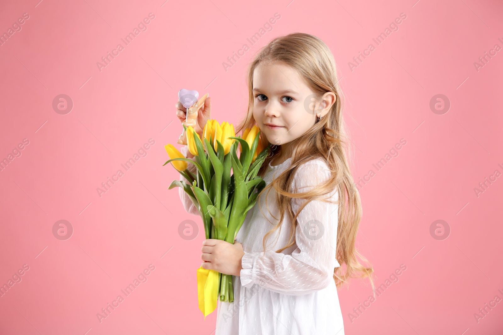 Photo of Cute little girl with yellow tulips and decorative bunny on pink background. Easter celebration