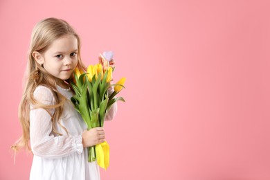 Photo of Cute little girl with yellow tulips and decorative bunny on pink background, space for text. Easter celebration