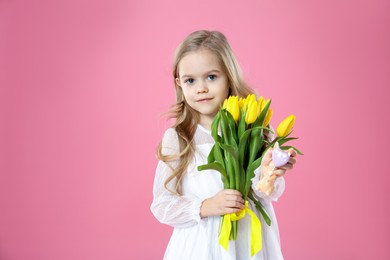 Photo of Cute little girl with yellow tulips and decorative bunny on pink background. Easter celebration