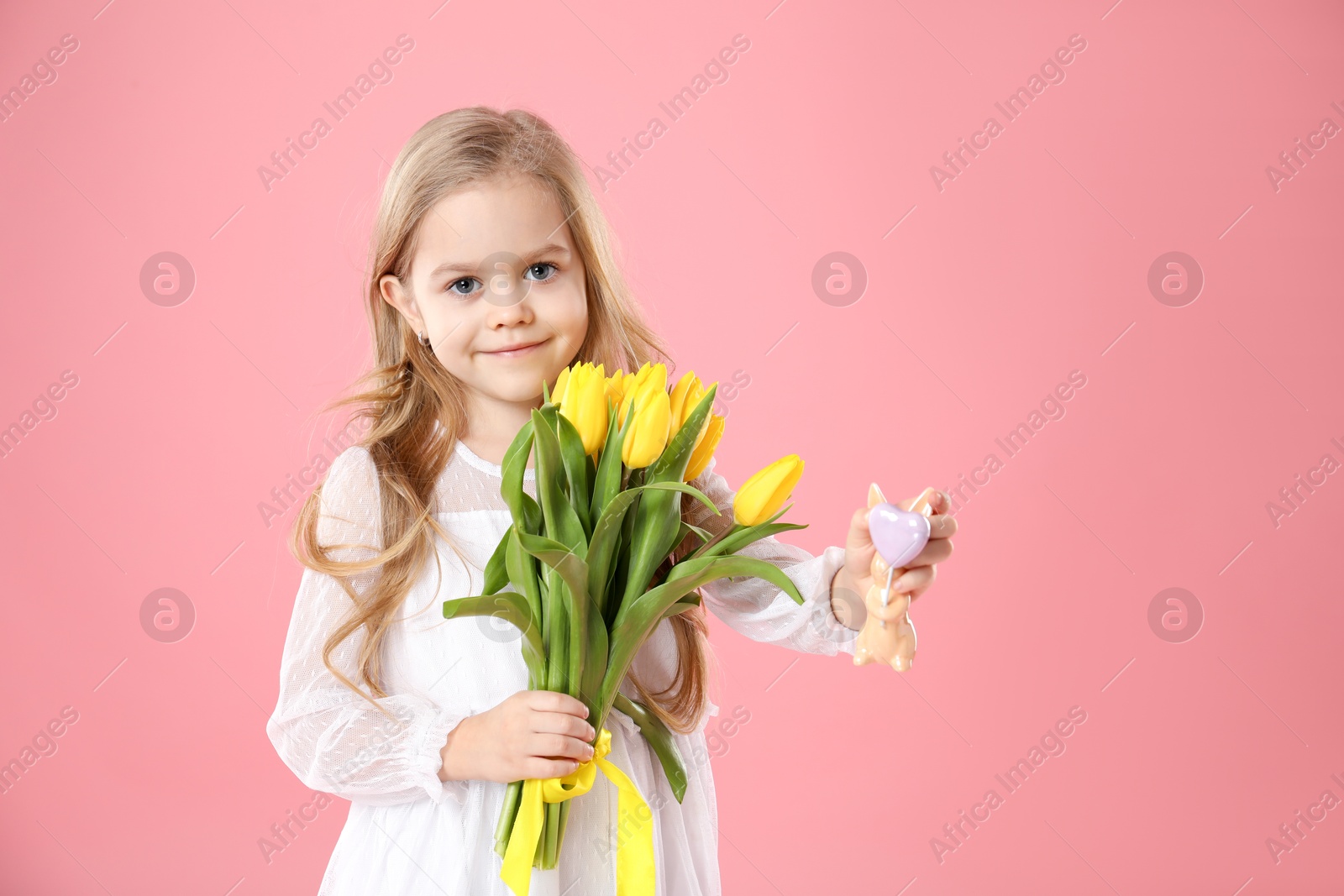 Photo of Cute little girl with yellow tulips and decorative bunny on pink background. Easter celebration