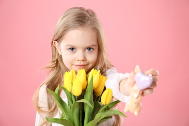 Cute little girl with yellow tulips and decorative bunny on pink background. Easter celebration