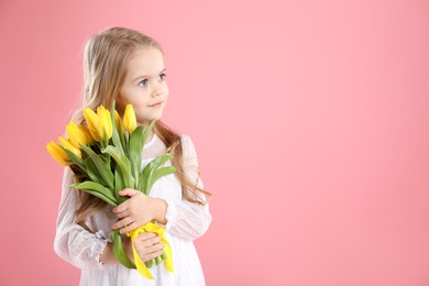 Photo of Cute little girl with beautiful yellow tulips on pink background, space for text. Spring season