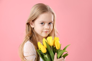 Cute little girl with beautiful yellow tulips on pink background. Spring season