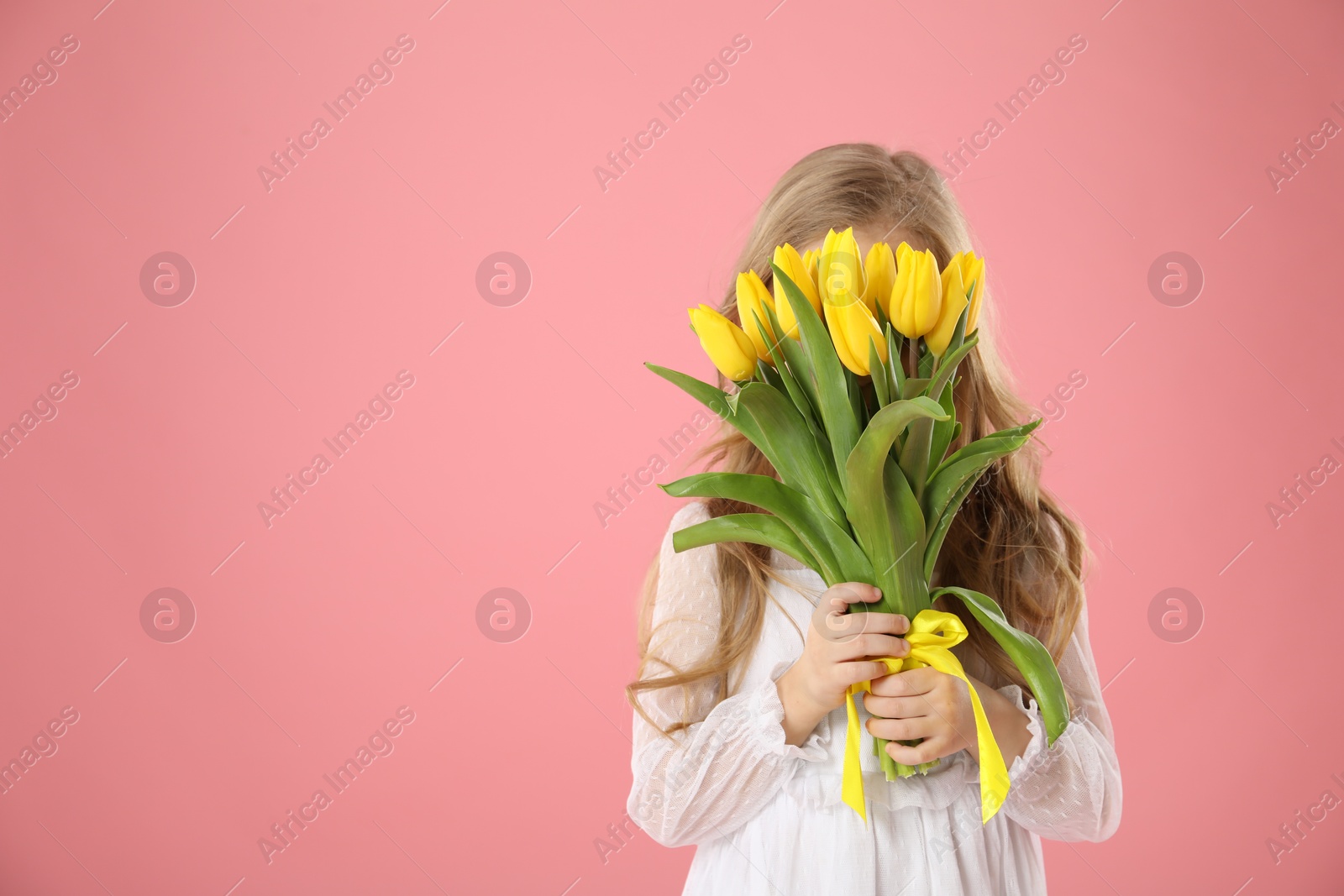 Photo of Little girl with beautiful yellow tulips on pink background, space for text. Spring season