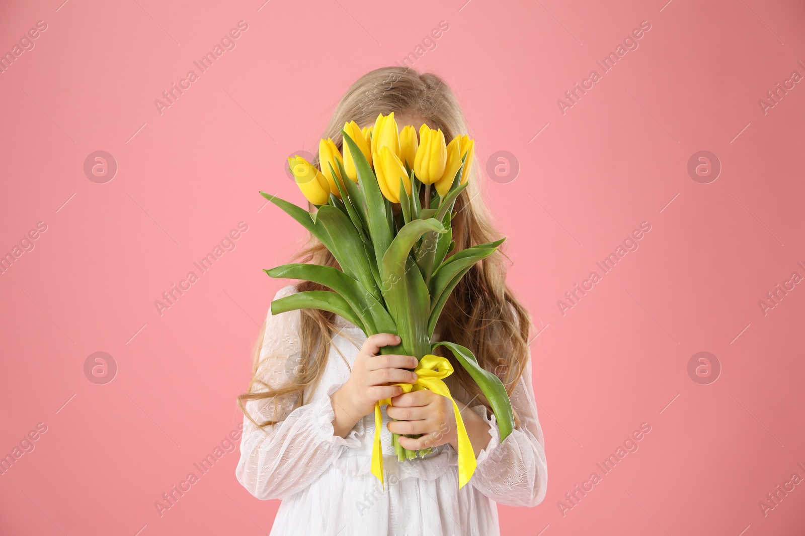 Photo of Little girl with beautiful yellow tulips on pink background. Spring season