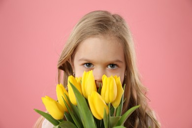 Cute little girl with beautiful yellow tulips on pink background. Spring season