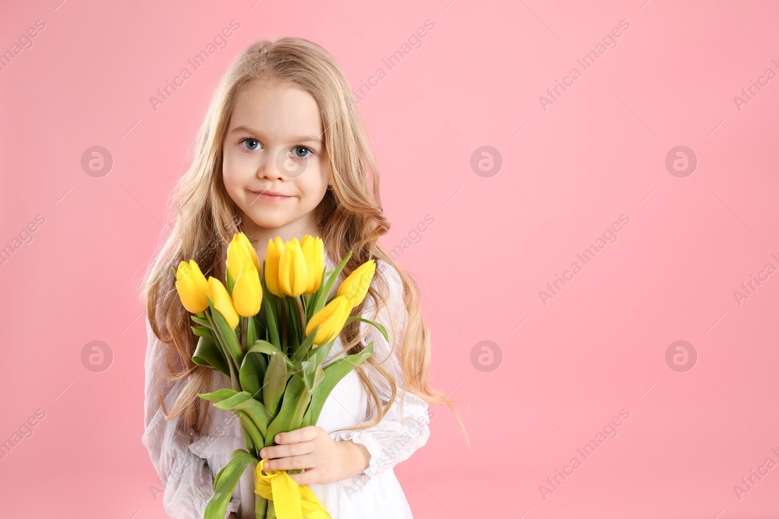 Photo of Cute little girl with beautiful yellow tulips on pink background, space for text. Spring season