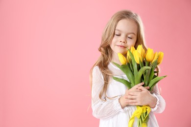 Cute little girl with beautiful yellow tulips on pink background, space for text. Spring season