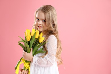 Cute little girl with beautiful yellow tulips on pink background, space for text. Spring season