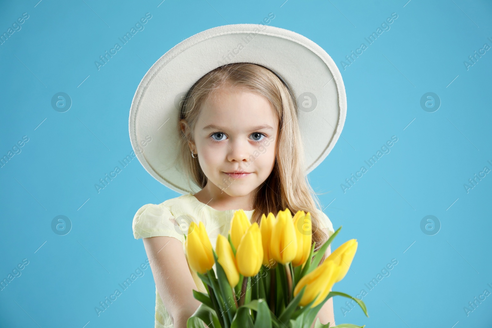 Photo of Cute little girl with beautiful yellow tulips on light blue background. Spring season