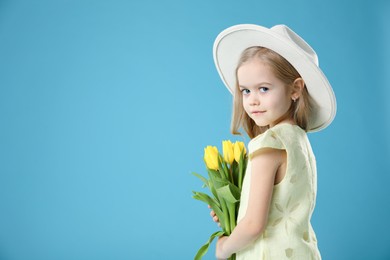 Photo of Cute little girl with beautiful yellow tulips on light blue background, space for text. Spring season