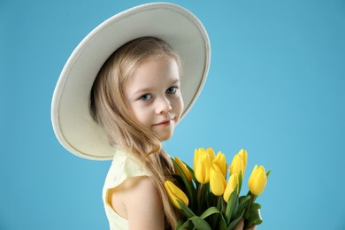 Photo of Cute little girl with beautiful yellow tulips on light blue background. Spring season