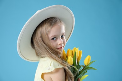 Cute little girl with beautiful yellow tulips on light blue background. Spring season