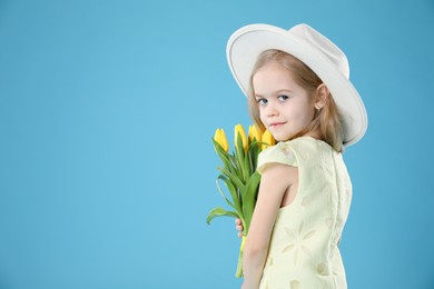 Cute little girl with beautiful yellow tulips on light blue background, space for text. Spring season