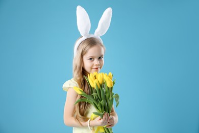 Cute little girl with bunny ears and tulips on light blue background. Easter celebration