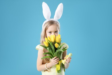 Cute little girl with bunny ears and tulips on light blue background. Easter celebration