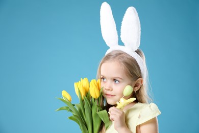 Photo of Cute little girl with bunny ears and tulips on light blue background. Easter celebration