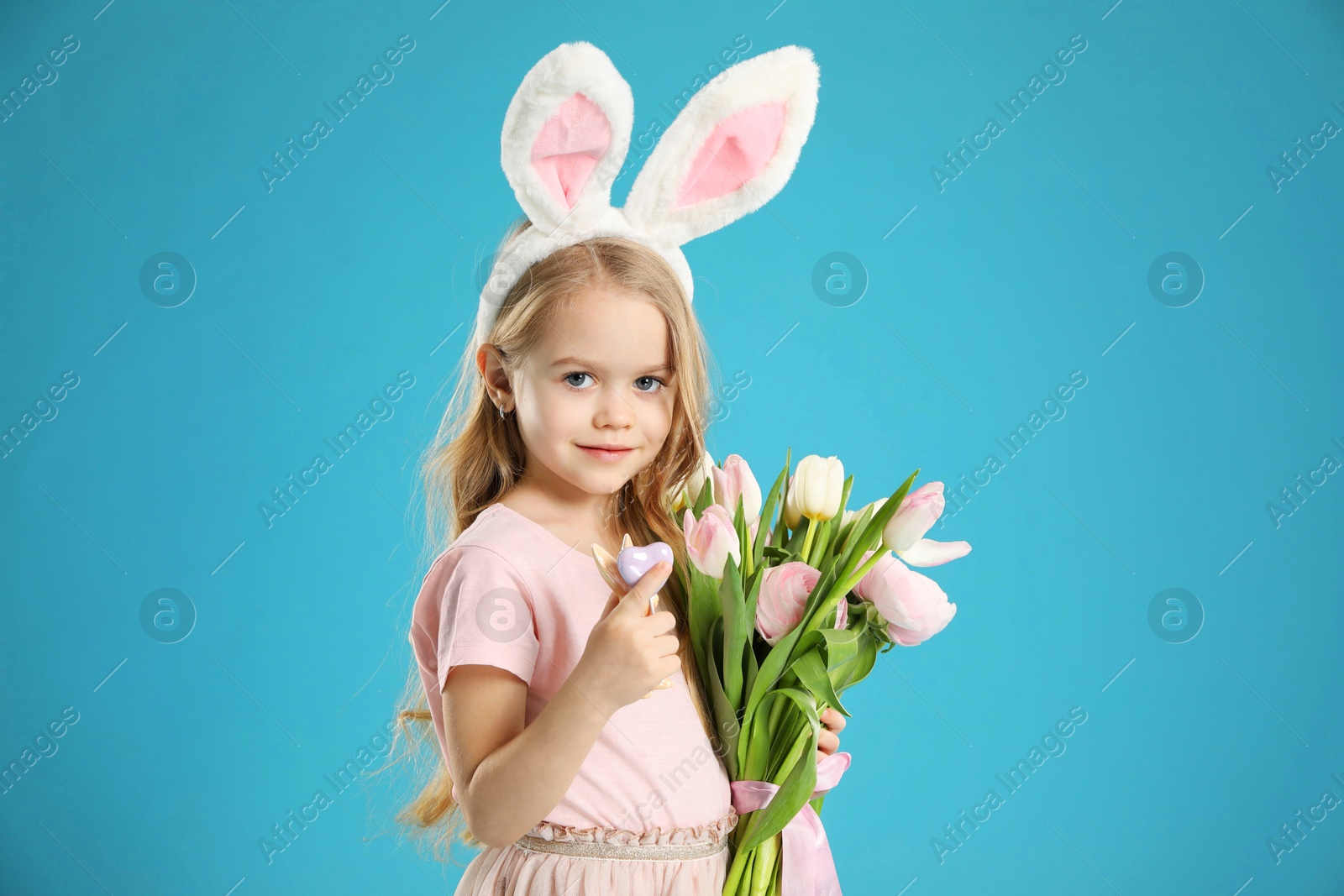 Photo of Cute little girl with bunny ears and spring flowers on light blue background. Easter celebration