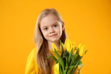 Cute little girl with beautiful yellow tulips on orange background. Spring season