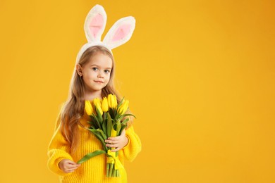 Photo of Cute little girl with bunny ears and tulips on orange background, space for text. Easter celebration